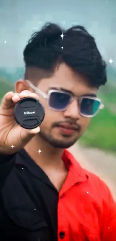 Young man holding camera lens on railway track wearing sunglasses.