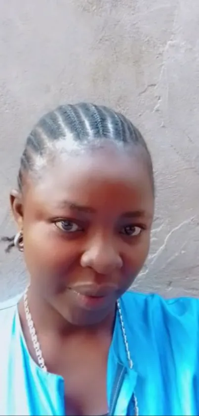 Woman with braided hair against a textured wall, wearing a blue top.