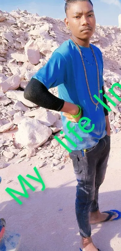 Man in blue shirt standing against rocky background, vibrant and stylish.