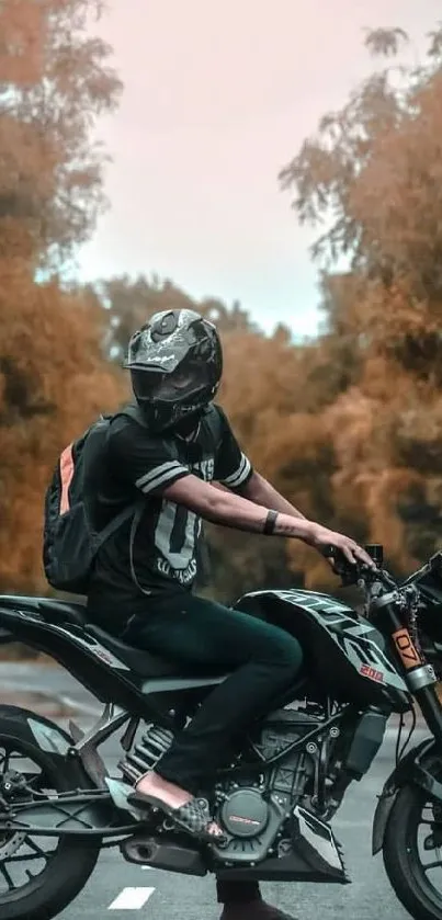 A biker rides on a road with orange autumn foliage around him.