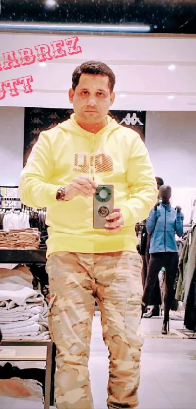 Man taking a selfie in a store mirror wearing a yellow hoodie and camo pants.