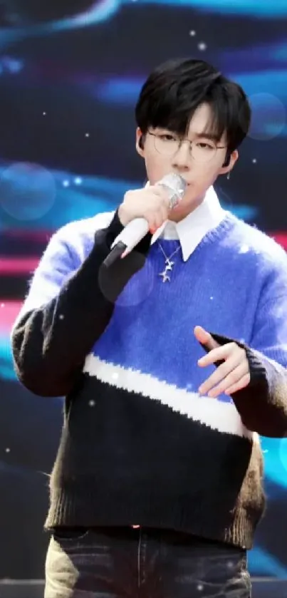 Singer with blue sweater performing on a vivid stage.