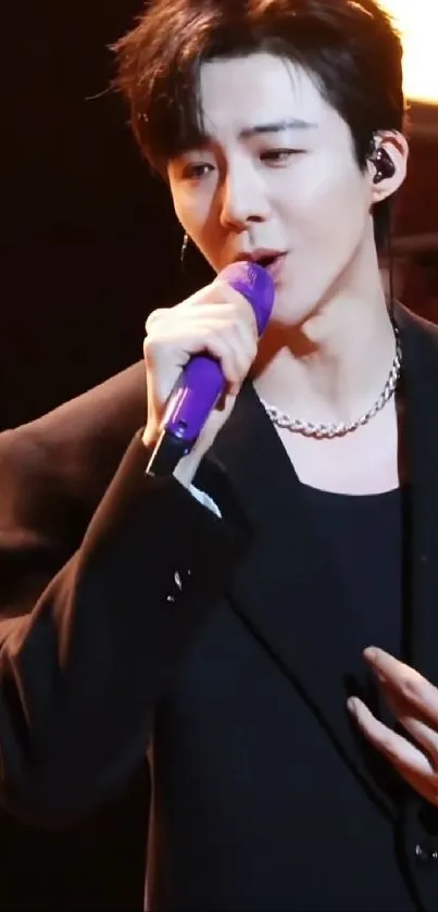 Singer in black suit with purple mic on stage.