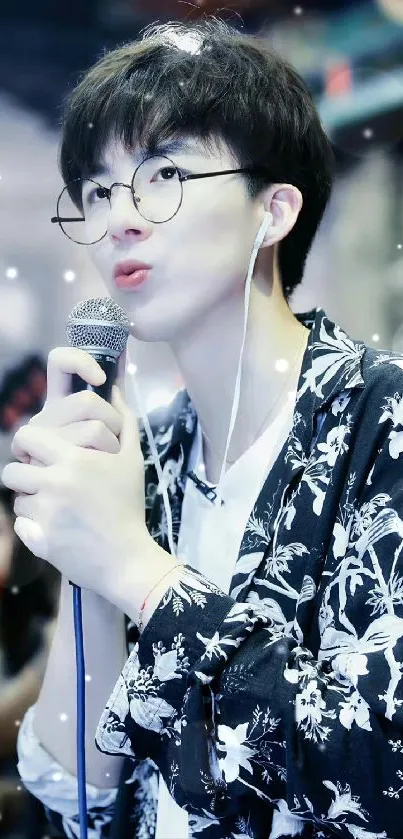 Stylish singer with glasses holding a microphone, wearing a floral shirt.