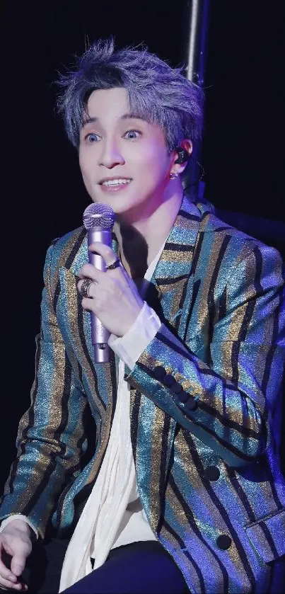 Stylish performer with shimmering outfit on stage, holding a microphone.