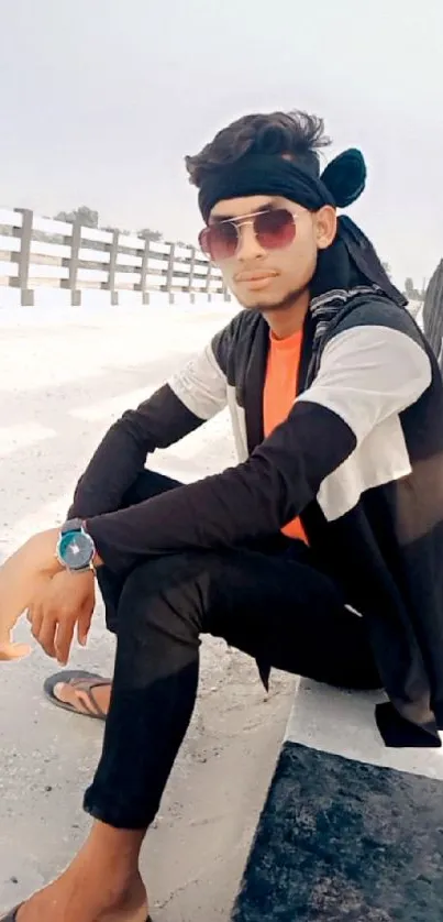 A young man in urban attire poses stylishly outdoors with sunglasses and a cool watch.