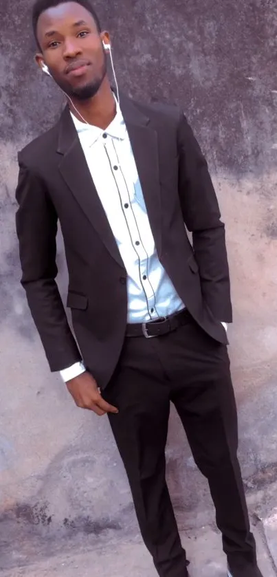 Man in black suit standing against a textured wall.