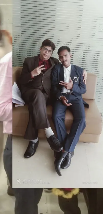 Two men in stylish suits sitting on a beige couch.