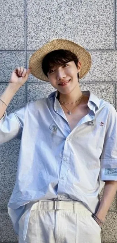 Person in straw hat and light blue shirt against a grey wall.