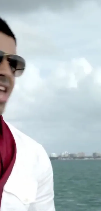 Man in sunglasses by the sea with a dramatic sky backdrop.