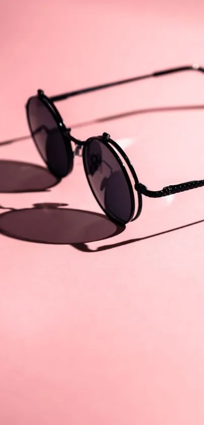 Round sunglasses casting shadow on pink background.