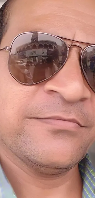 Man wearing sunglasses reflecting a cityscape in close-up view.