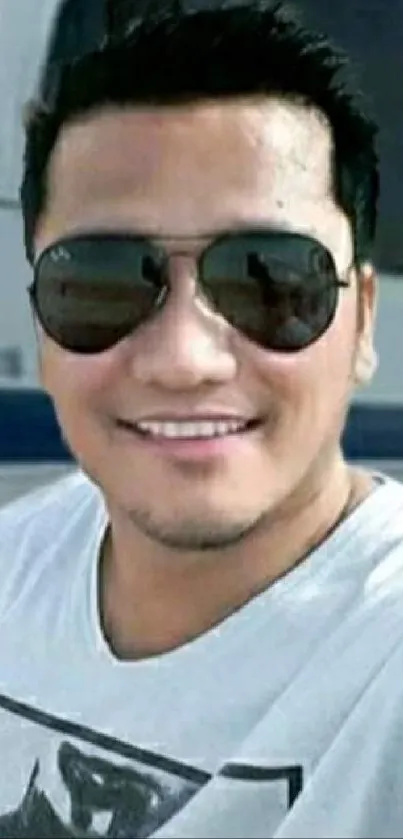 Person wearing sunglasses smiles in outdoor selfie with modern backdrop.