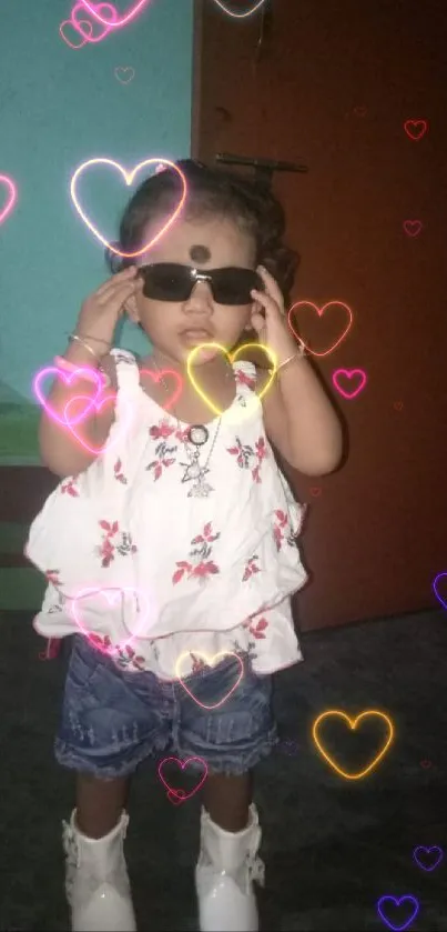 Toddler in floral outfit and sunglasses posing confidently indoors.