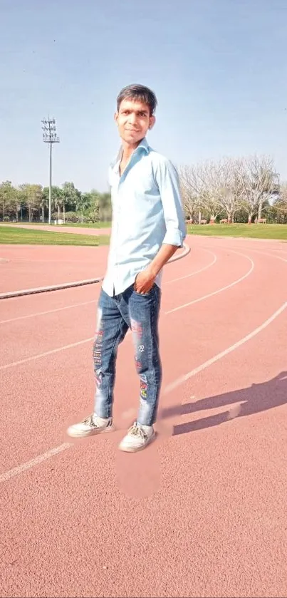 Man in blue shirt on a track field under clear sky.