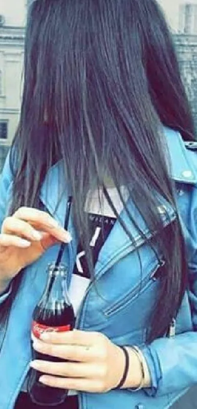 Young woman in blue leather jacket holding a drink.