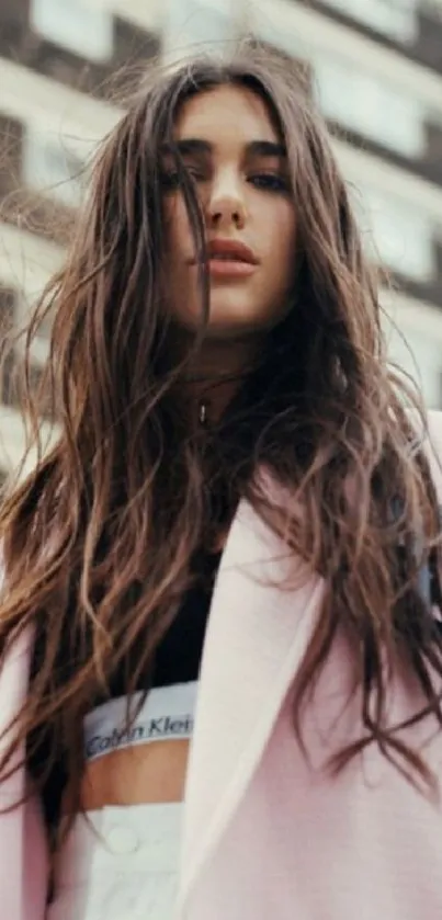 Woman with flowing hair in urban setting wearing light pink jacket.