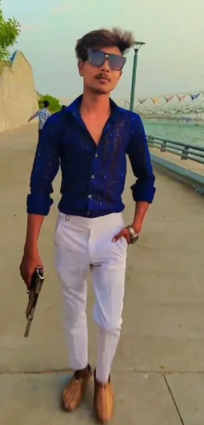 Man in blue shirt and white pants posing by a riverside walkway.