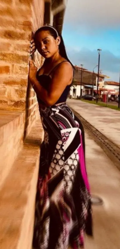 Woman in colorful dress leaning against brick wall in an urban setting.