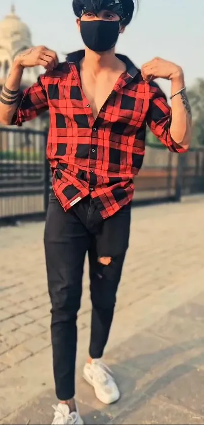 Person in red plaid shirt and black jeans in urban setting.