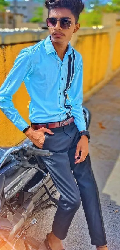 Young man in sunglasses posing by a vibrant yellow wall with a motorcycle.