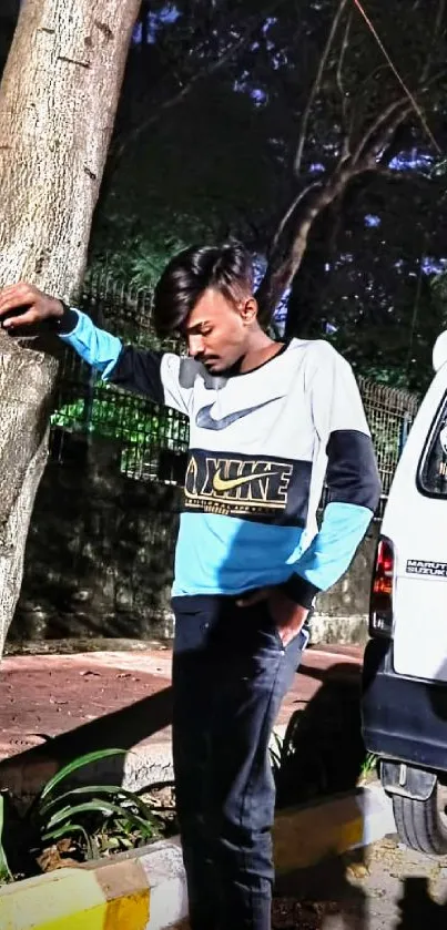Man in streetwear leaning against a tree.