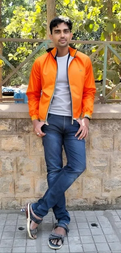 Person in orange jacket posing against stone wall.