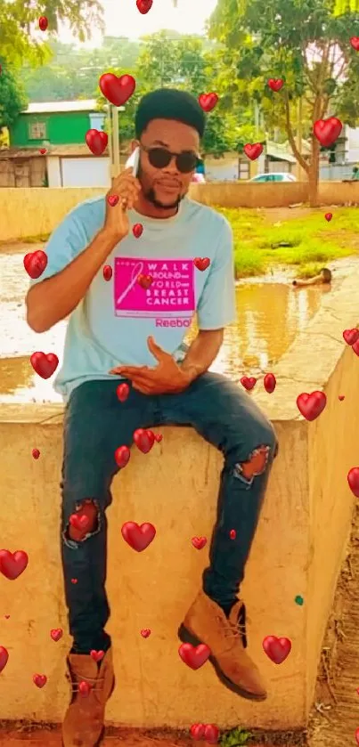 Man in urban attire sitting outdoors by a pond.