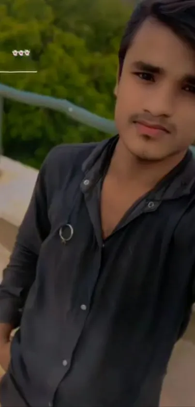 Young man in casual attire outdoors, with greenery backdrop.