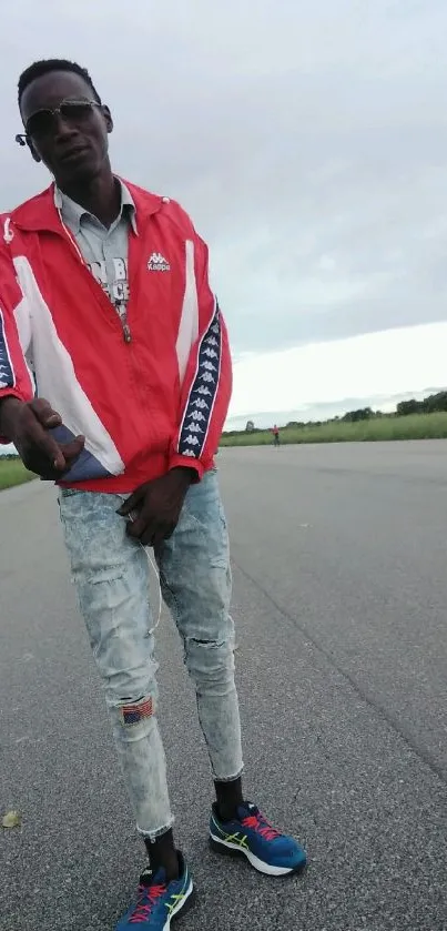 Stylish person wearing a red jacket on a road under a cloudy sky.