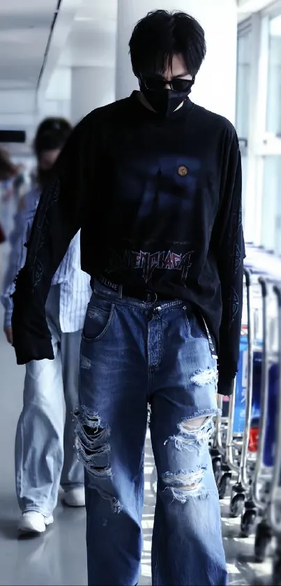 Man in stylish streetwear with ripped jeans in a bright hallway.