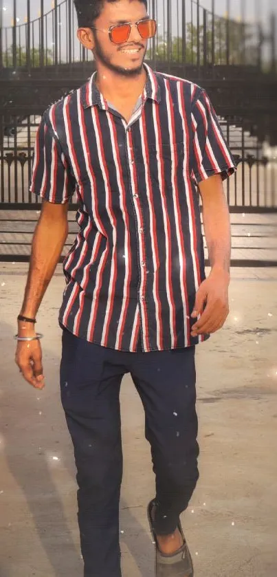 Person wearing stylish striped shirt with sunglasses, walking outdoors.