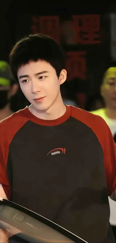 A young man in a red and gray t-shirt, standing on a street at night, cool urban vibe.