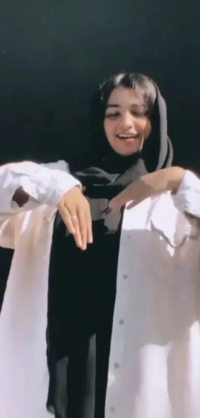 Woman wearing a black hijab and white shirt, creating a heart symbol with her hands.