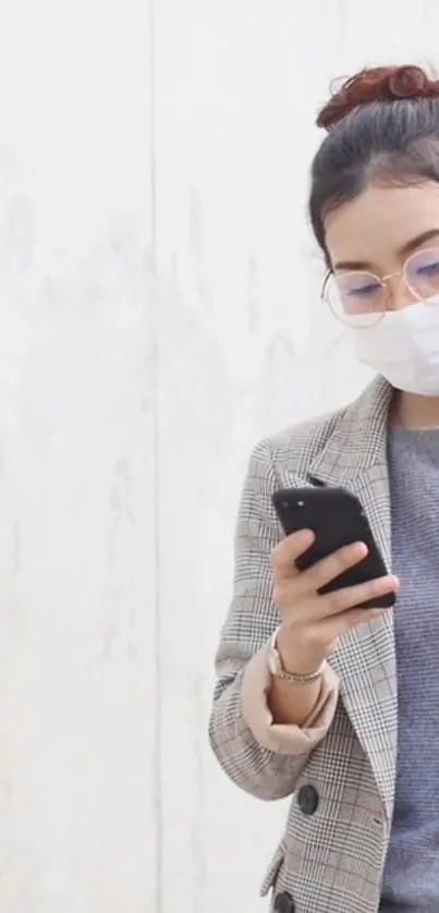 Woman in plaid coat using smartphone against light gray wall.