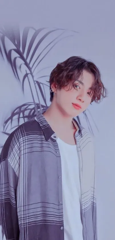 Young man in casual shirt with wavy hair and plant backdrop.