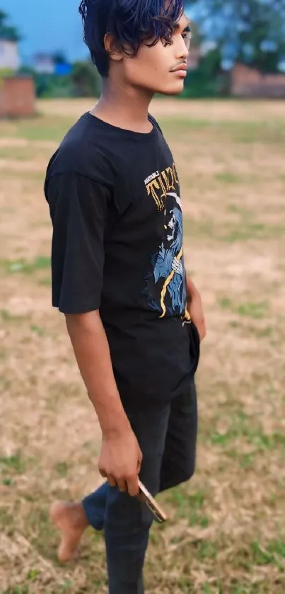 Young man in black outfit standing in a grassy outdoor setting.