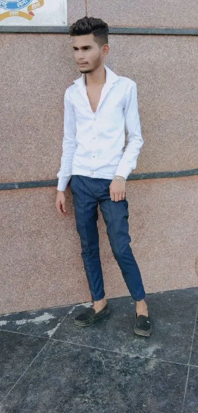 Young man in stylish outfit posing against a textured brown wall.