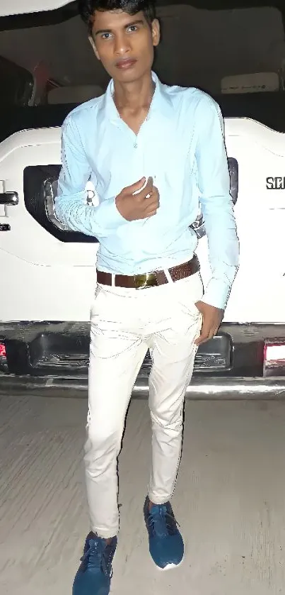 Young man in blue shirt and white pants standing by a vehicle.