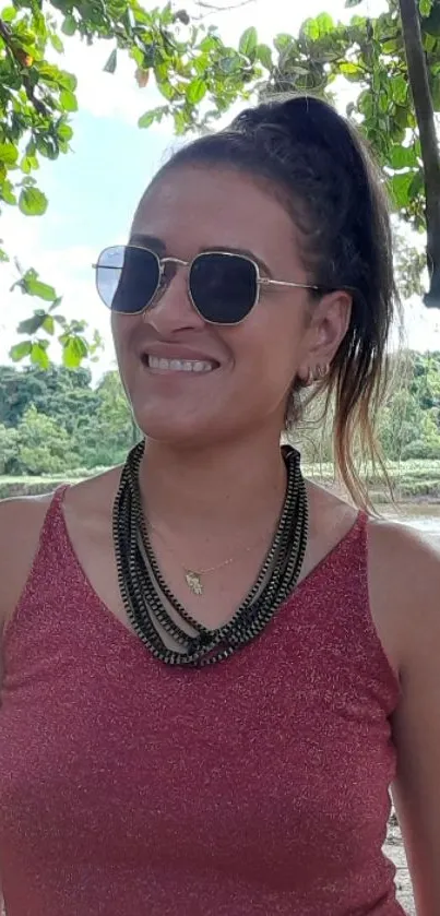 Smiling woman in sunglasses with lush green background.