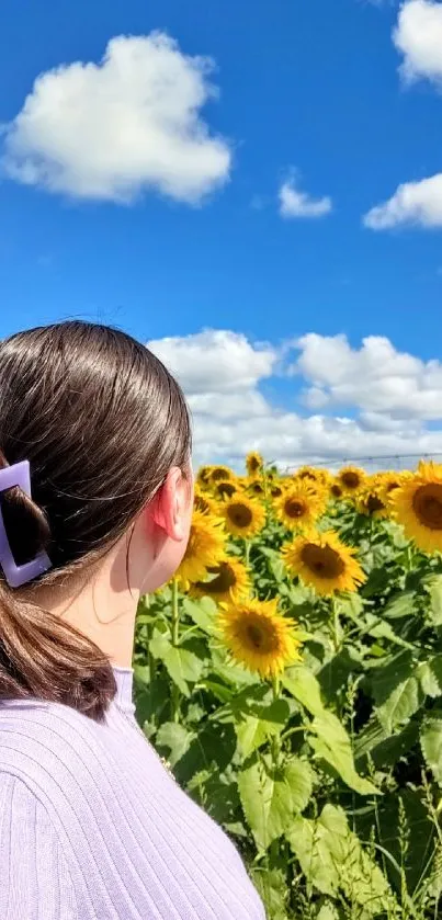 Woman looks at sunflowers under a blue sky.