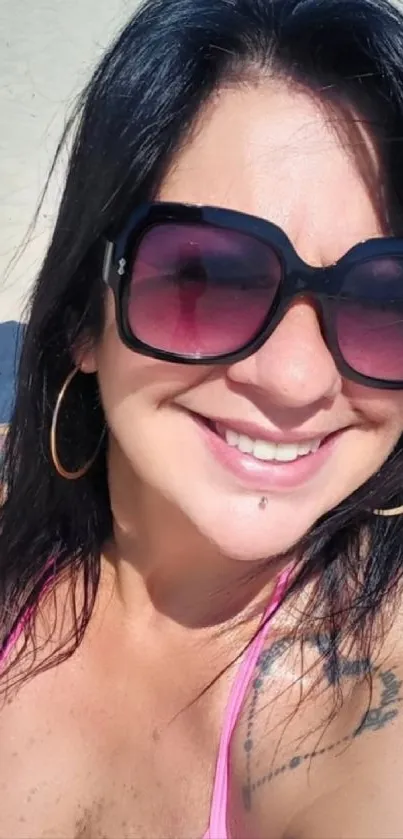 Woman smiling on a sunny beach with sunglasses.