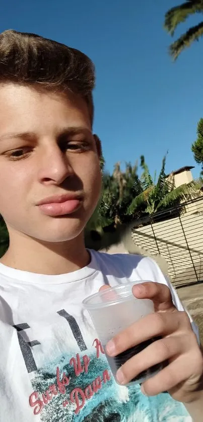 Youthful person holding a drink outside with a blue sky backdrop.