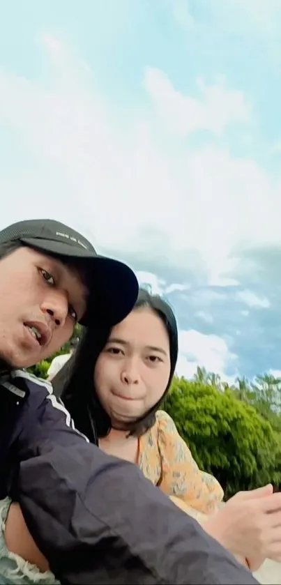 Selfie with clear blue sky and lush greenery in the background.