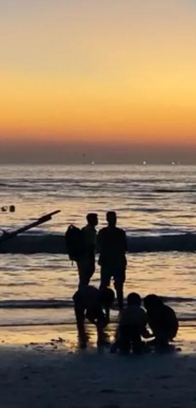 Silhouettes on a sunset beach with orange sky and calm ocean waves.