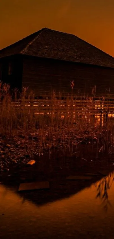 Lakeside cabin at sunset with orange sky.