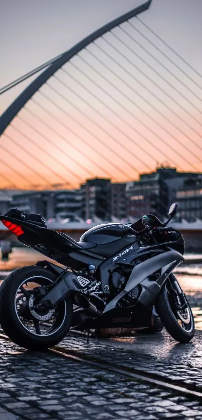 A sleek motorcycle parked by a city harbor at sunset, under a modern bridge.