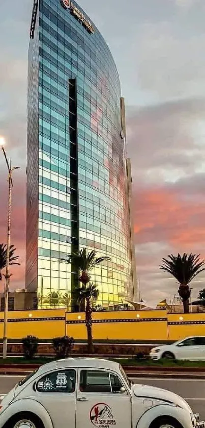 Vintage car on a city street with a modern glass building at sunset.