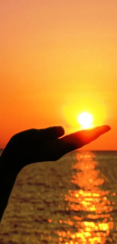 Hand holds the sun in a vibrant orange sunset over the ocean.