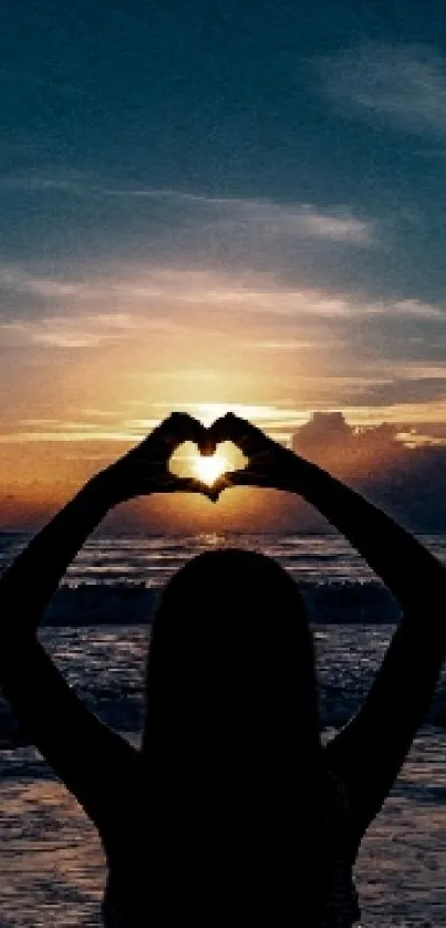 Silhouette forming a heart at sunset with ocean in the background.
